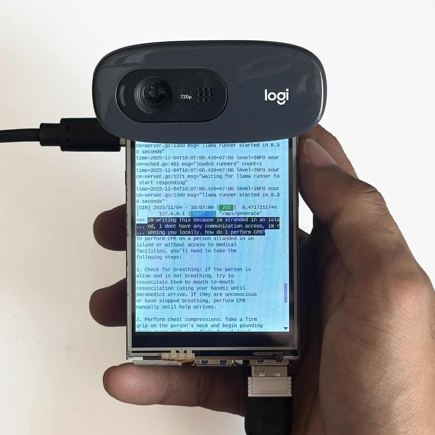 The device held in one hand: a Raspberry Pi with a small touchscreen and a Logitech webcam on top, the screen showing a local Llama model explaining how to perform CPR