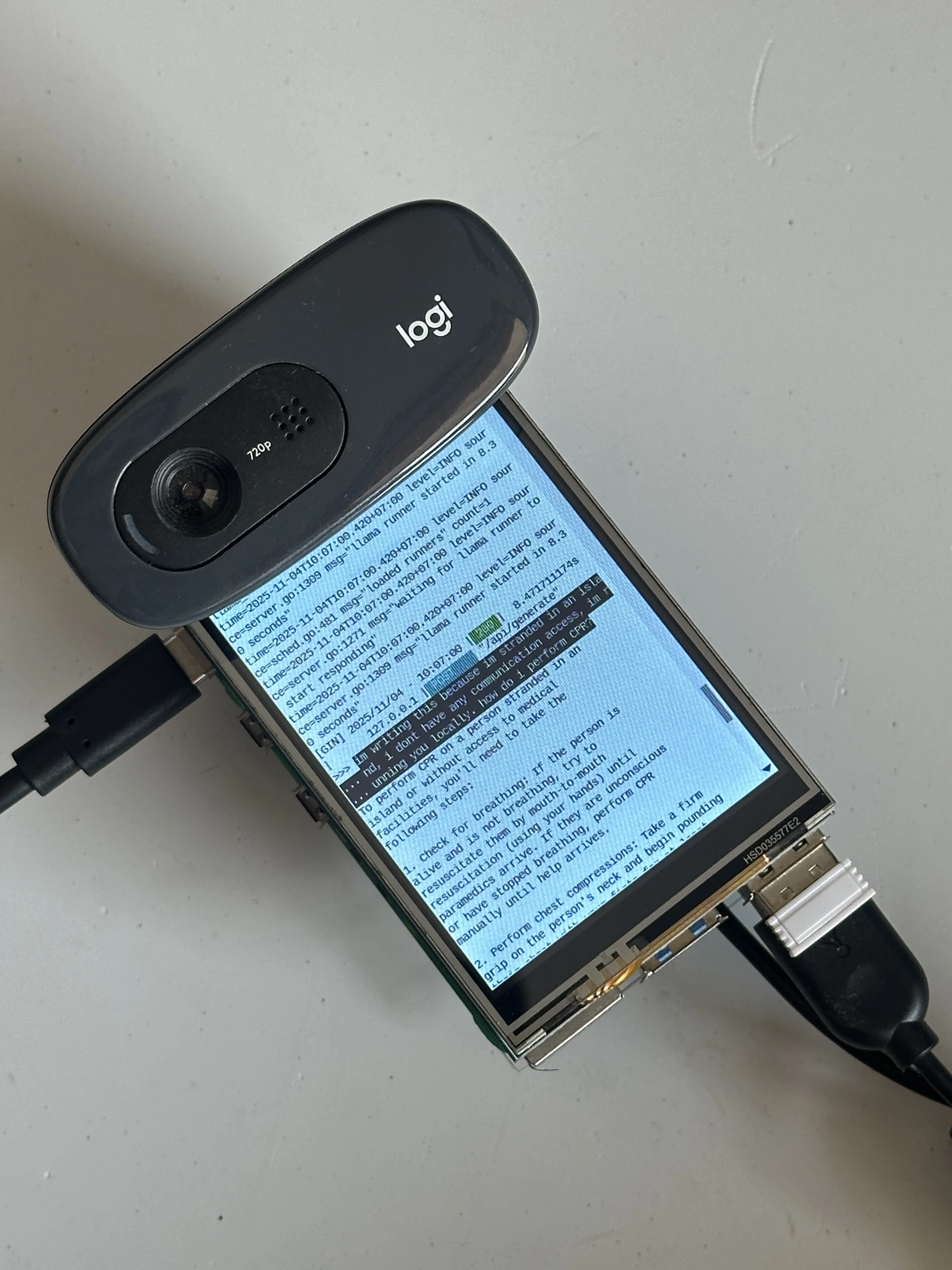 The device on a table, its webcam on top: the model answers a question typed from a stranded island with no communication access, explaining how to perform CPR