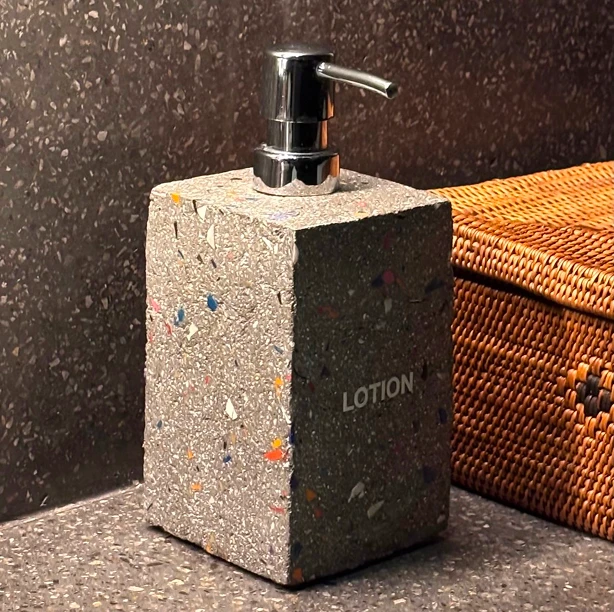 A terrazzo-like concrete lotion dispenser flecked with coloured plastic, next to a rattan box